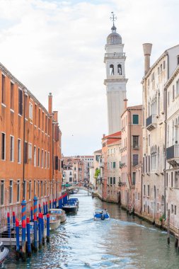 The Venice canal with boats, bright stilts and a tall tower in the background