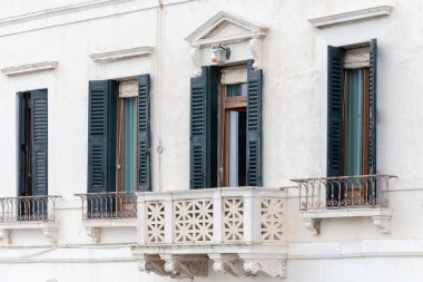 Yeşil panjurlu ve dekoratif balkonlu beyaz bir bina.