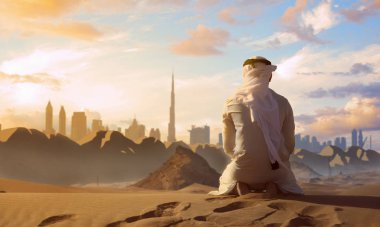 Arabic man with traditional emirates clothes praying in the UAE desert front Dubai skyline. clipart
