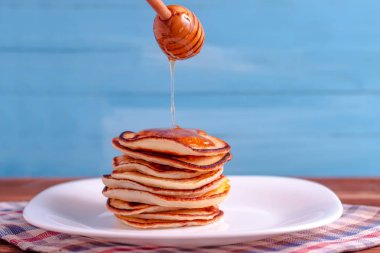 Beyaz arka plan karşı tabakta bal lezzetli ince katlanmış krep üzerine dökülen