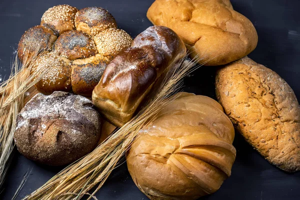 Sortiment čerstvě upečených chlebů s pšeničným uchem na černém pozadí. Mělká Hloubka pole. — Stock fotografie