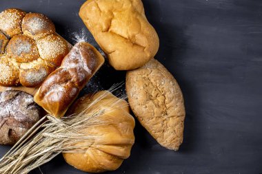 Siyah arka plan üzerinde buğday kulakları ile taze pişmiş ekmek çeşitleri. Sığ alan derinliği.