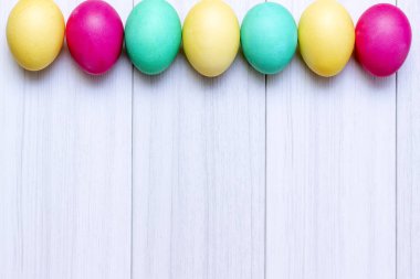 Paskalya yumurta beyaz ahşap zemin üzerinde pastel renklerde boyanmış.