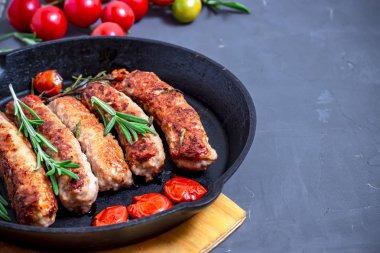 Siyah taş zemin üzerinde ızgara sosis ve kiraz domatesleri. Üst manzara, düz uzanma.