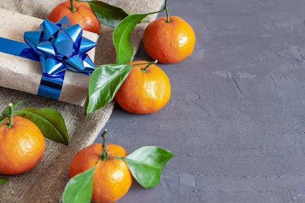 Christmas gift box on a dark background and tangerines. New Year\'s attributes.