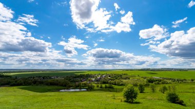 Bulutlu mavi gökyüzüne karşı yeşil tepeler.