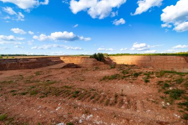 Terk edilmiş kum kuyusu. Arkaplanda bulutlu mavi bir göl var.