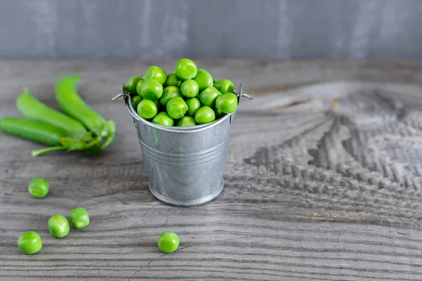 暗い木製のテーブルの上に小さな金属製のバケツで新鮮な緑のエンドウ豆のクローズアップビュー. — ストック写真