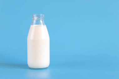 Mavi arka planda izole edilmiş bir şişe taze süt.