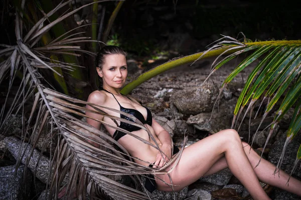 검은 수영복에 이상적인 시체와 함께 섹시 한 젊은 여자는 정글에서 종 려 잎에 포즈 — 스톡 사진