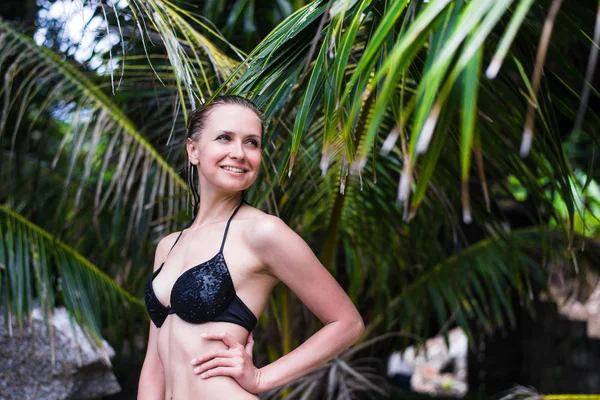 Gros plan de la jeune fille mince sexy debout sur une plage portant maillot de bain bikini noir avec feuille de palme verte sur le fond. Elle est bronzée et élégante . — Photo