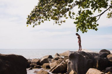 Açık deniz ile tropikal beach yakınındaki bir kayada duran genç zarif uygun kadın portresi. Spor kız bikini zevk doğa yaz tatili, Tayland deniz