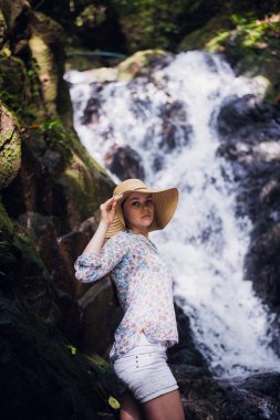 Sevimli kadın tarafından orman şelaleler poz bir şapka ile