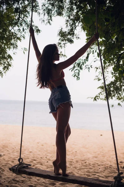 タイのビーチで海にぶら下がってスイングに帽子立っている美しい少女 — ストック写真