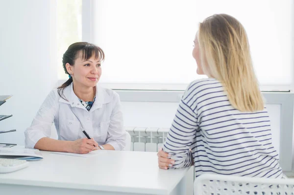 Paciente sonriente que recibe una consulta médica y mira a la cámara, la doctora está sentada en el escritorio en el fondo — Foto de Stock