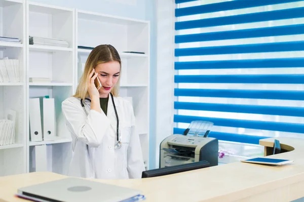 Ritratto di una bella infermiera sorridente alla scrivania mentre parla al telefono e compila un modulo di informazioni mediche — Foto Stock
