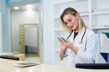 Gülümseyen bir bodur giyen ve hastane resepsiyonda çalışan kadın doktor, o bir Pano bir tıbbi rapor yazma ve randevuları zamanlama