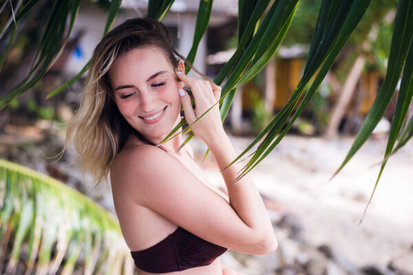 A beautiful young woman with long blonde hair posing on a beach dressed in sexy bikini top. She enjoys the wind and flirting with camera.