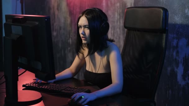 Gamer girl seating in front of the computer playing online game. Young woman is very concentrated while playing computer esport tournament. She talking with her team usiang a microphone — Stock Video