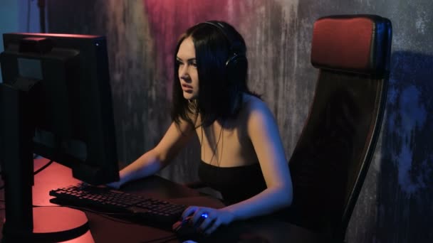 Mulher séria desfruta de vitória em um jogo de vídeo. Gamer menina jogando jogo online em um computador pc usando fone de ouvido e falando com uma equipe usando microfone — Vídeo de Stock