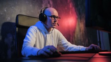 Genç adam online oyun arkadaşları ile başlar. Erkek oyun gülümseyen ve giyen kulaklık ve mikrofon kullanarak bir ekip ile konuşurken bir pc bilgisayar online oyun oynamak