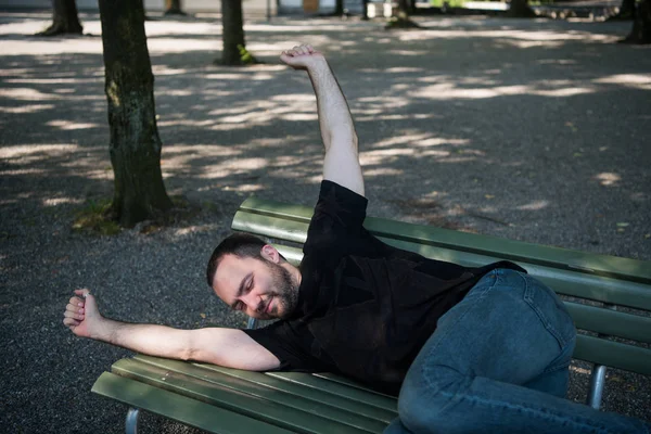 Молодий чоловік лежить спати на лавці в парку і прокидається після відпочинку — стокове фото
