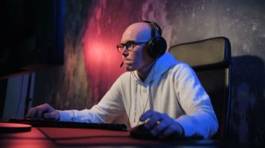 Genç adam giyen kulaklık ve online oyun arkadaşları ile başlar. Erkek oyun gülümseyen ve online oyun pc bilgisayarınızda yürütmekte ve mikrofon kullanarak bir ekiple konuşuyor