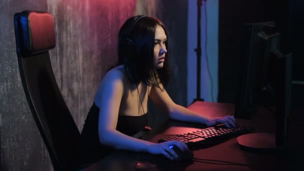 Girl gamer in headphones and with mouse and keyboard in her hands playing network games preparing to participate in international competitions in e-sports — Stock Video