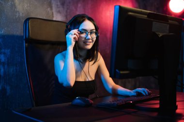 Gözlük ve oyun kulaklık giyen güzel genç kız online oyun karanlık alanı içinde Pc oyun üzerinde çalış. Internet üzerinde akış online oyunlar