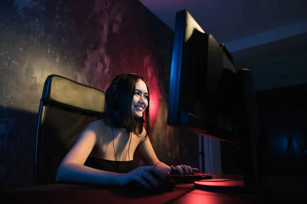 Une jolie gamer féminine s'assoit dans une pièce confortable derrière un ordinateur et joue à des jeux. Femme en direct des jeux vidéo en streaming à ses fans. Streamer et gamer concept — Photo