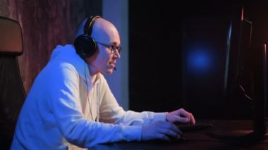 Kulaklıklı Mutlu Adam evdeki masaüstü bilgisayarında oyun oynuyor.