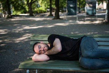 Genç adam uzanıp parkta bankta uyuyor ve dinlendikten sonra uyanıyor.