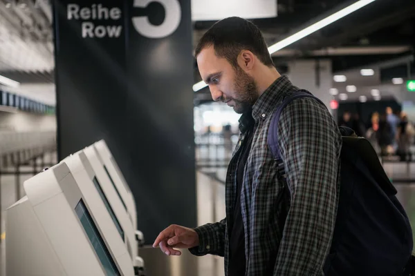 Jonge man met rugzak aanraken interactieve weergeven met behulp van Self-Service-machine, zelf-check-in doen voor de vlucht of het kopen van vliegtickets op automatische inrichting in moderne luchthaven terminal gebouw — Stockfoto