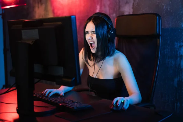 Gritando emocional jovem mulher zangada jogando no computador pessoal segurando teclado jogo e mouse sentado em uma cadeira em casa. Gaming gamers conceito . — Fotografia de Stock