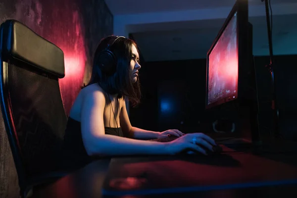 Una linda chica gamer se sienta en una acogedora habitación detrás de una computadora y juega juegos. Mujer streaming en vivo videojuegos para sus fans. Streamer y concepto de jugador —  Fotos de Stock