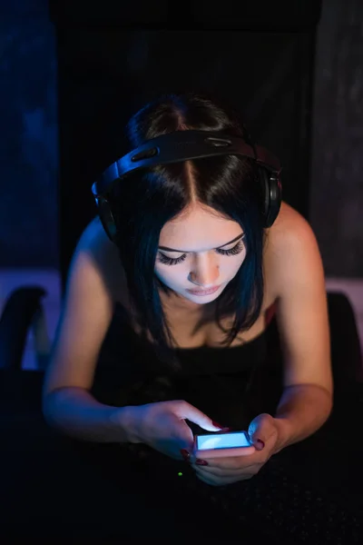 Ansicht von oben: hübsches Mädchen entspannt sich zu Hause, sie spielt Musik mit einem Smartphone und trägt schwarze Kopfhörer. — Stockfoto