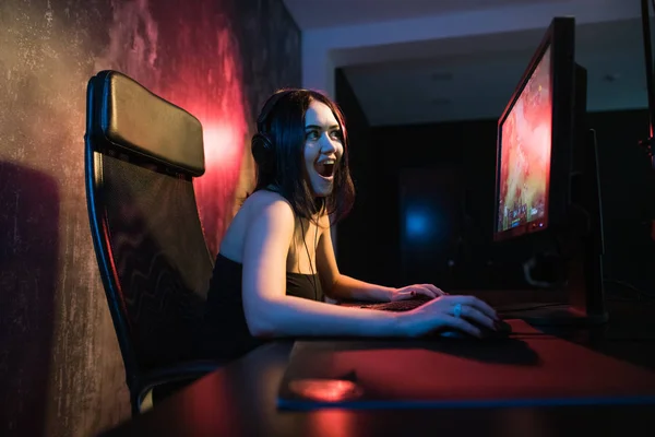 Una linda chica gamer se sienta en una acogedora habitación detrás de una computadora y juega juegos. Mujer streaming en vivo videojuegos de ordenador a sus fans y mover la mano a ellos. Streamer y concepto de jugador . —  Fotos de Stock