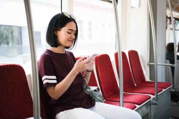 Retrato al aire libre de una joven hermosa mujer usando su teléfono móvil en un autobús . — Foto de Stock
