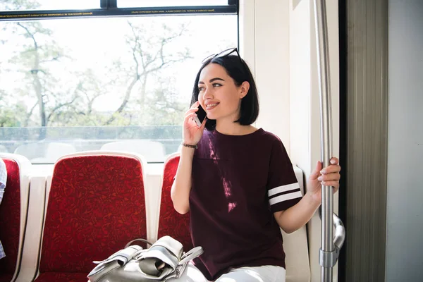 Joven mujer feliz sentada en el autobús de la ciudad y hablando por teléfono móvil . — Foto de Stock