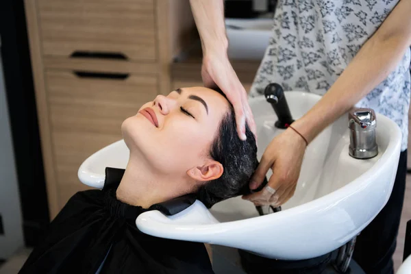 Beauty and people concept - happy young woman with hairdresser washing head at hair salon — Stock Photo, Image