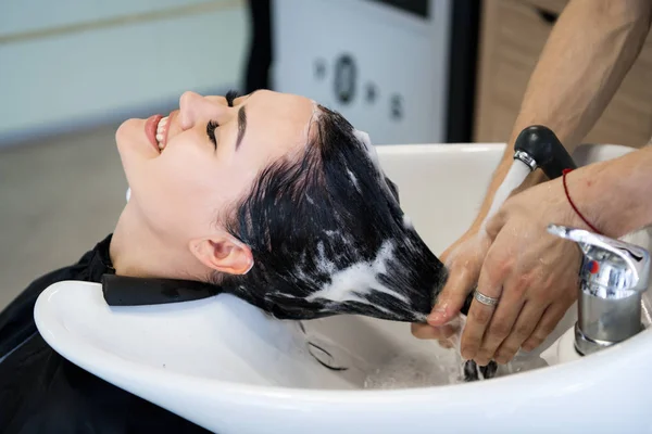 Haircare procedure in beauty salon. Hairdresser is brushing womans hair spreading a treatment mask or conditioner — Stock Photo, Image