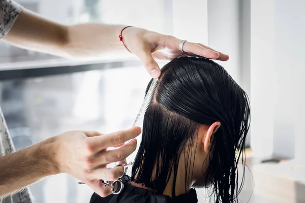 Penata rambut pria tersenyum dan berbicara dengan seorang pelanggan sambil membuat potongan rambut baru untuk wanita berambut cokelat muda yang cantik — Stok Foto