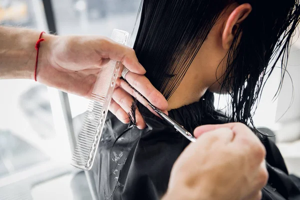 O cabeleireiro faz um corte de cabelo com tesoura de cabelo para uma jovem em um salão de beleza . — Fotografia de Stock