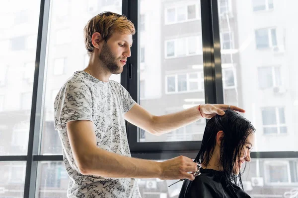 O cabeleireiro faz um corte de cabelo com tesoura de cabelo para uma jovem em um salão de beleza . — Fotografia de Stock