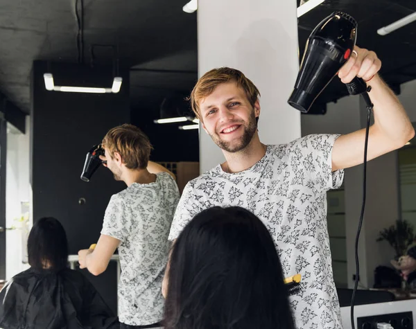Επαγγελματική χαμογελώντας αρσενικό στυλίστας χτύπημα στέγνωμα γυναικεία μαλλιά με πιστολάκι σε κομμωτήριο — Φωτογραφία Αρχείου