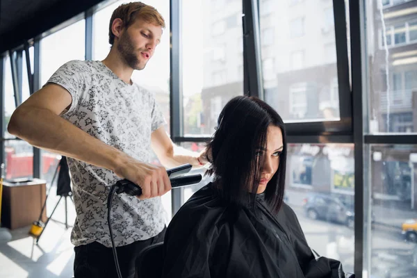 Mulher bonita feliz enquanto cabeleireiro está alisando seu cabelo no salão. Novo corte de cabelo ou penteado para mulher jovem . — Fotografia de Stock