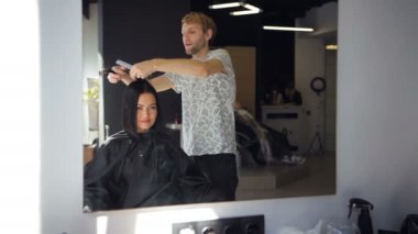 Erkek profesyonel kuaför saç salonda bir hairstraightener kullanarak esmer kadının saç düzleştirme