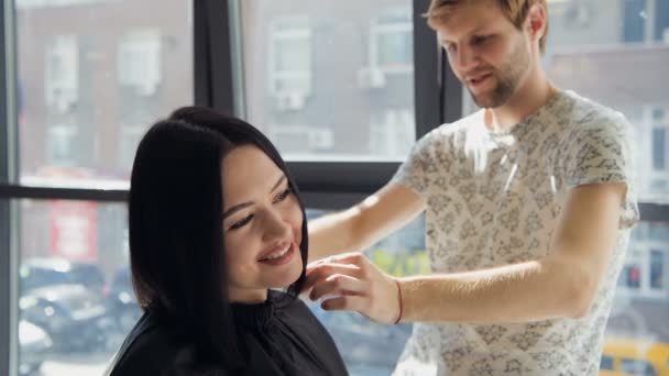 Uma mulher em um salão de cabeleireiro esperando para ver os resultados olhando em um espelho, sorrindo e conversando com o artista — Vídeo de Stock