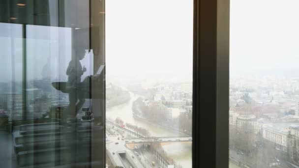 Рефлексия человека, идущего по рельсам в тренажерном зале на высоком этаже с прекрасным видом на город с автомобильным движением на дороге — стоковое видео
