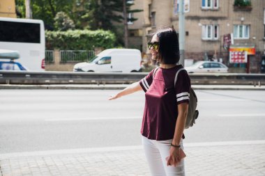 Taksi durdurmak için yol yakın dururken el hareketi güneş gözlüklü Genç Sevimli gülümseyen kadın. Güzel hippi kız toplu taşıma açık havada yakalamak.